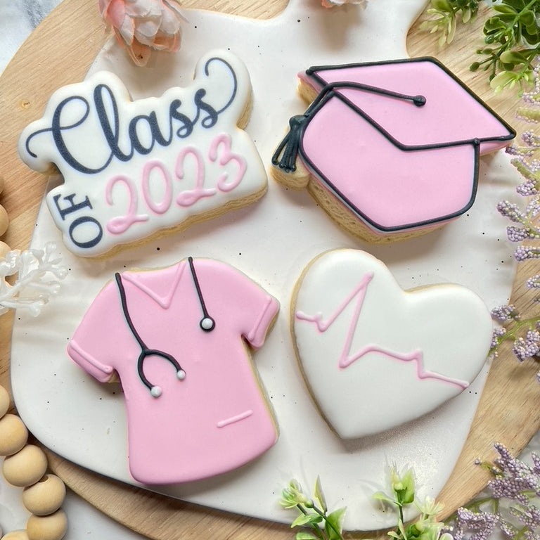 Custom Class of 2023 nursing graduation cookie set featuring a pink graduation cap, nurse's scrub, heartbeat heart, and 'Class of 2023' message