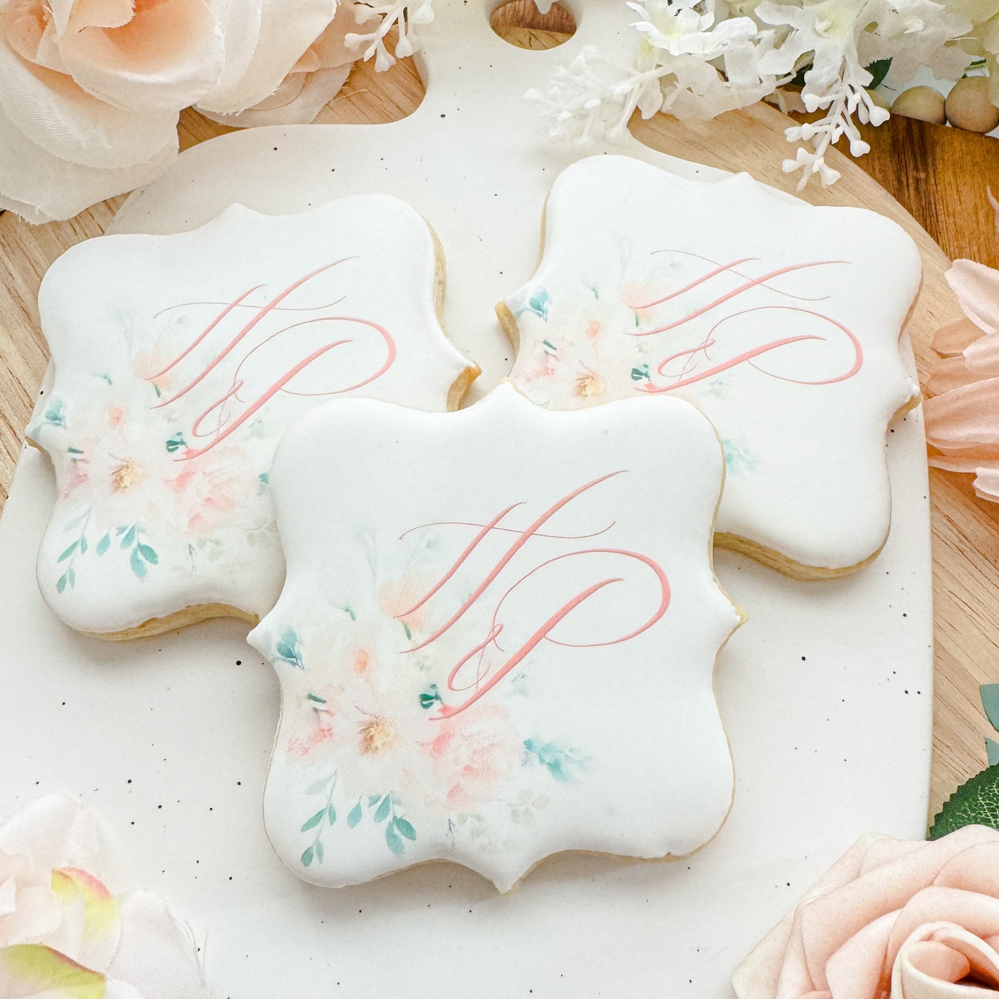 Square sugar cookies decorated with a pink monogram and a floral watercolor design in shades of pink and green.
