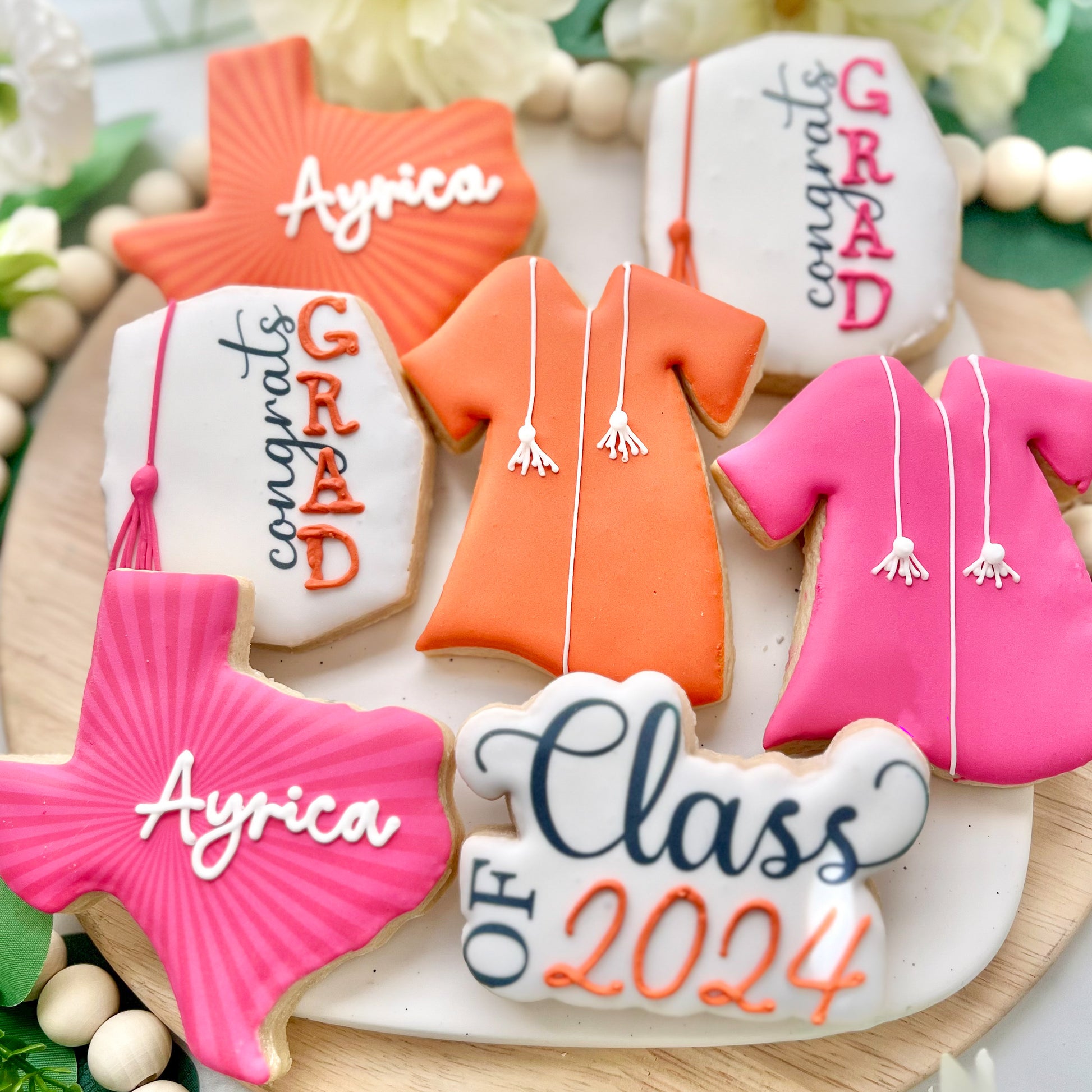 Custom Texas-themed graduation cookies for the Class of 2024 featuring Texas shapes, grad gowns, and celebratory plaques in pink, orange, and white.
