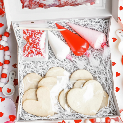 Heart-shaped cookies in a decorative box with baking tools on a red and white heart-themed background.