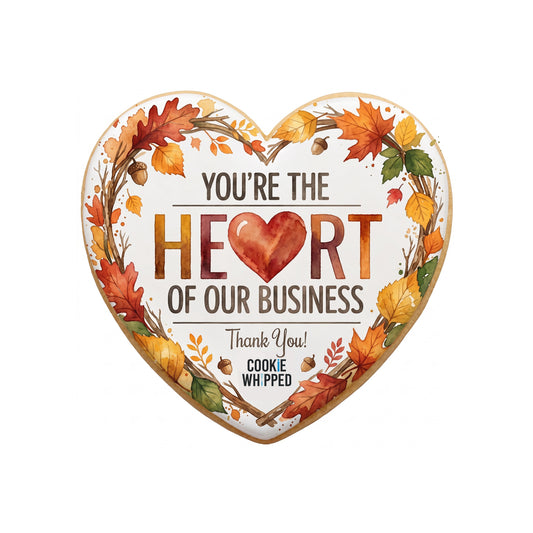 A heart-shaped sugar cookie with cream royal icing base featuring the printed sentiment 'Heart of Our Business' in warm fall script with subtle autumn leaf accents.