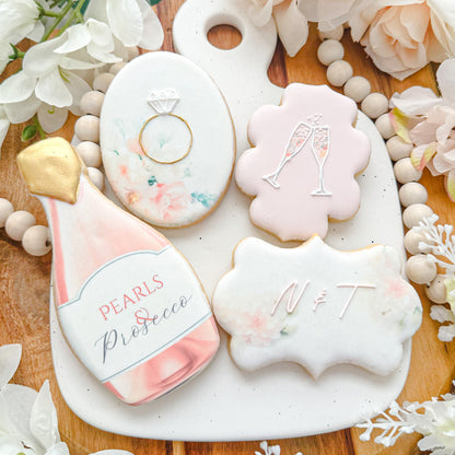 Four decorated cookies on a white platter. Designs include a pink champagne bottle, a floral oval with a ring, two champagne glasses on a pink background, and a floral rectangle with the letters "N & T."Bridal Shower, Sugar cookie,  Floral,  Muted & soft,  Oval,  Circle, Rectangle, Plaque,  Box,  Gift-box,  Simply Cute,  Printed,  Edible Image
