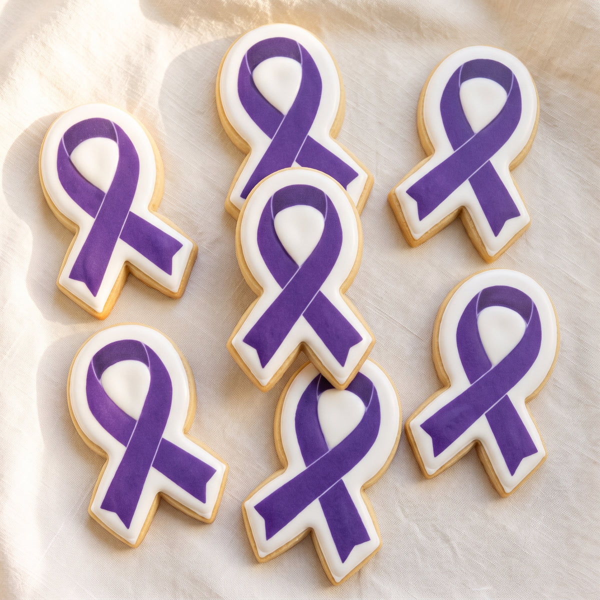 A ribbon-shaped sugar cookie with a solid white icing base and a deep royal purple awareness ribbon printed on top with a clean white border frame.