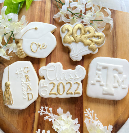 Custom Texas A&M graduation cookies in white and gold featuring graduation caps, logos, and celebratory "Class of 2022" plaques.
